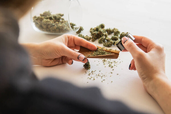 Крупным планом марихуаны с молотилкой. Женщина закатывает тупую марихуану на белом фоне. Концепция использования конопли. Женщина готовит и катит марихуану марихуану.
.