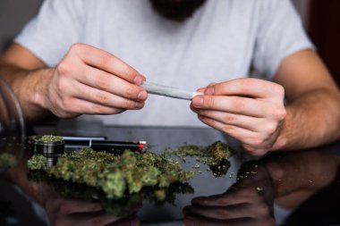 Uyuşturucu narkotik konsepti. Kapatın. Esrar saran bir adam. Uyuşturucu kullanımı. Marihuana hazırlayan ve yuvarlayan adam. Marihuanayı çakmakla yakan bağımlıya yakın..
