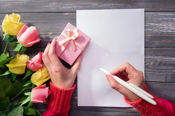Ahşap masa üzerinde bir pembe hediye kutusu tutan kadının el. kadın yazacak.
