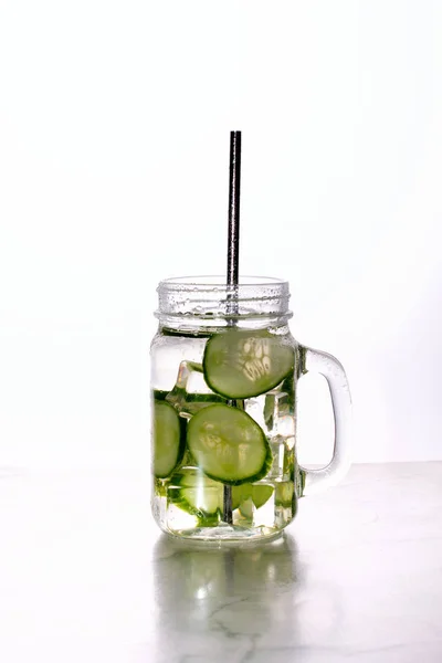 Glass of cucumber water with ice on white background.