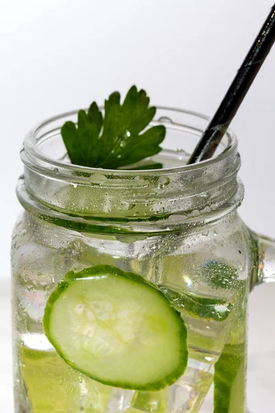 Glass of cucumber water with ice on white background.