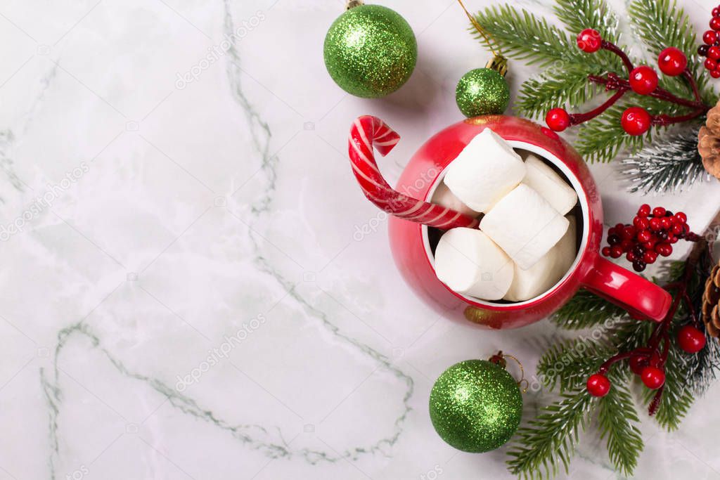Christmas drink. Red mug with hot chocolate and marshmallows on a marble background. Christmas balls and branches of spruce. Candy cane. Top view