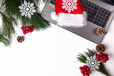 Ofis beyazı masa, bilgisayar, çam dalı ve Noel Baba şapkası. Noel arkaplanı. Boşluğu kopyala.