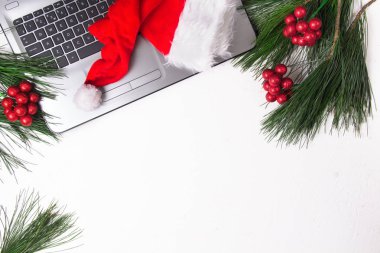 Ofis beyazı masa, bilgisayar, çam dalı ve Noel Baba şapkası. Noel arkaplanı. Boşluğu kopyala.
