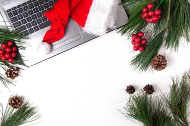 Ofis beyazı masa, bilgisayar, çam dalı ve Noel Baba şapkası. Noel arkaplanı. Boşluğu kopyala.