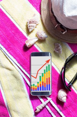 Finansal programı olan bir akıllı telefon, bir plaj havlusu, güneş gözlüğü ve deniz kabukları. İş çizelgesi. Tatilde serbest çalışan.