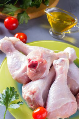 Maydanozlu çiğ tavuk budu ve gri arka planda domatesler. Kırsal biçim. 