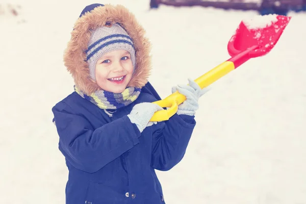 Дитина грає зі снігом з лопатою взимку . — стокове фото