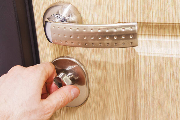 The man's hand closes the lock on the door. Turn the door latch.