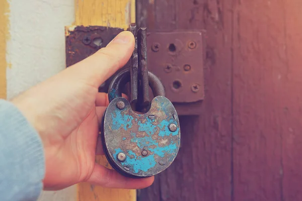 Una mano humana sostiene una vieja cerradura vintage sobre el fondo de una vieja puerta de madera . — Foto de Stock