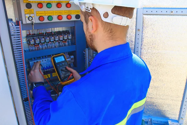 electrical engineer with a multimeter performs adjustment work in the blurred control cabinet