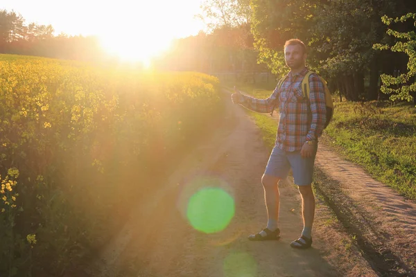 Путешественник идет пешком по зеленой луговой дорожке с рюкзаком большой палец вверх яркий солнечный свет — стоковое фото