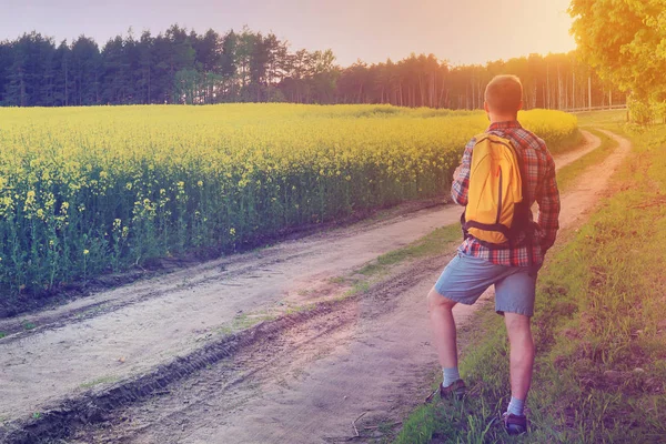 Um viajante com uma mochila aguarda o caminho no campo para um passeio — Fotografia de Stock