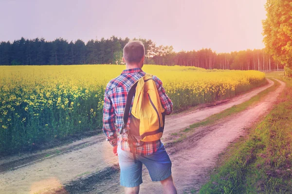 Junger Reisender allein auf der Straße in Feld Blick voraus bei Sonnenuntergang — Stockfoto