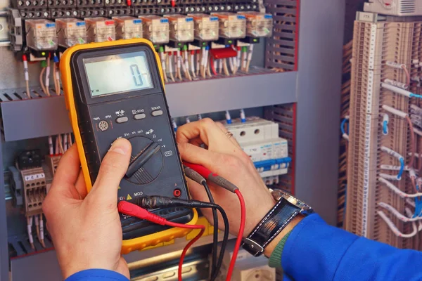 Meetinstrument in handen van een close-up van de elektricien op een onscherpe achtergrond van elektrische elementen. — Stockfoto