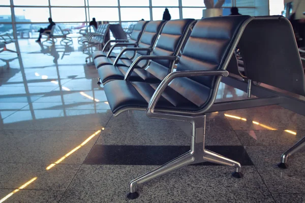 Los asientos en la sala de espera del aeropuerto sobre el fondo de las siluetas de los pasajeros — Foto de Stock