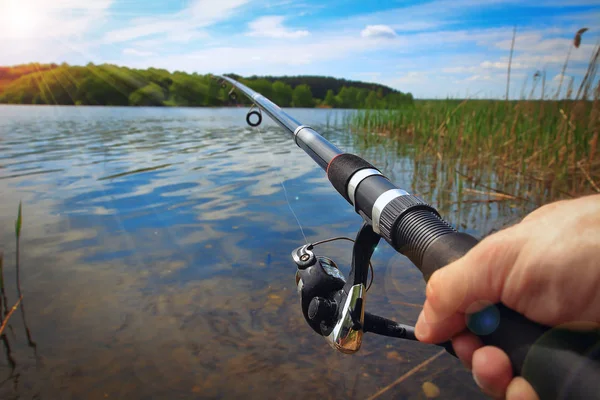Canne à pêche et les mains du pêcheur sur l'eau du lac — Photo