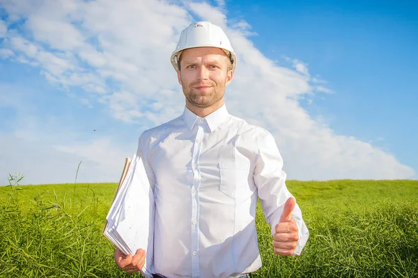 Ingenieur architect bouwer houdt zijn duim omhoog. Ontwerper in wit helm tekeningen in handen — Stockfoto