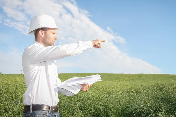 Ingenieur-architect met tekeningen in wit helm verwijst naar site van bouwplaats — Stockfoto