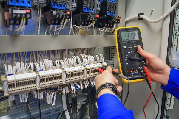 En manos del multímetro electricista en el fondo del armario eléctrico de cerca . — Foto de Stock