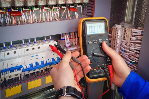 Multimeter is in handen van elektricien op achtergrond van elektrische automatisering kabinet. — Stockfoto