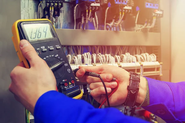 Multimeter in hands of electrician close-up against  background of electrical wires and relays