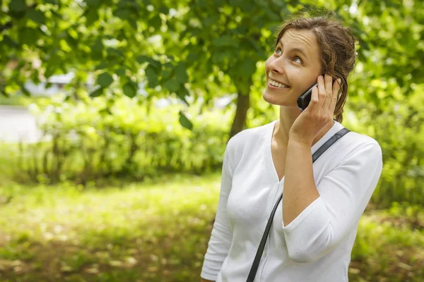 Beautiful young girl is calling by phone in green summer park — Stock Photo, Image