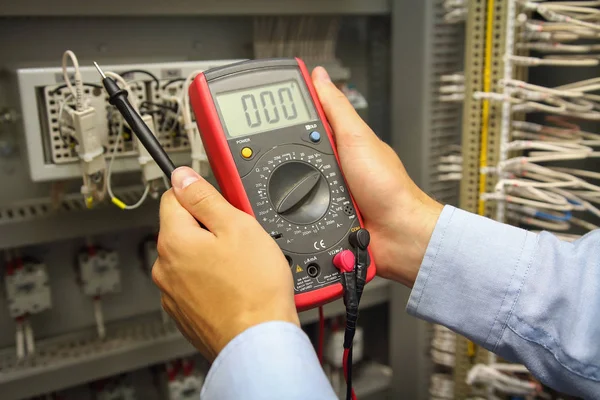 Multímetro em mãos de engenheiro elétrico no fundo do painel de controle de automação . — Fotografia de Stock