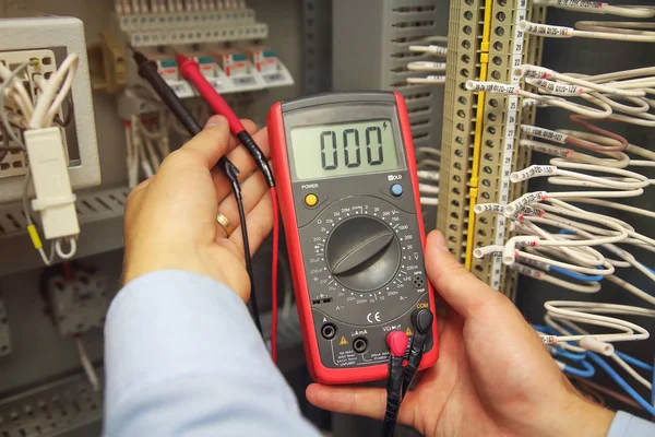 Ingeniero prueba circuitos eléctricos industriales con multímetro en caja de terminales de control. Manos del ingeniero con multímetro de primer plano sobre el fondo de las filas terminales del panel de automatización — Foto de Stock