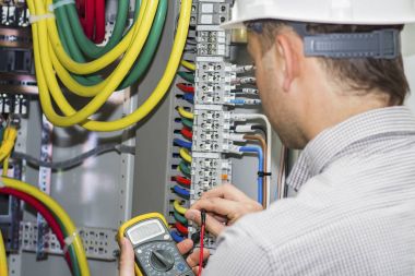 Mühendis kaynağı devre dağıtım kablo Klemens kutusuna arka plan üzerinde güçlü panelinde sınar. Elektrikçi multimetre ile sigortaları gerilim ölçer