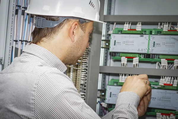 El ingeniero monta el controlador para la automatización de procesos en el armario de control. Electricista en casco blanco ajusta caja tecnológica de automatización industrial . — Foto de Stock