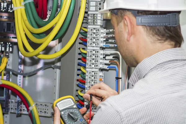 Engineer tests supply circuit in powerful panel of distribution cables on terminal box background. Electrician with multimeter measures voltage in fuse box Stock Image