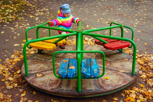 Barn rider karusell i lekplats under hösten. Liten flicka som leker. — Stockfoto