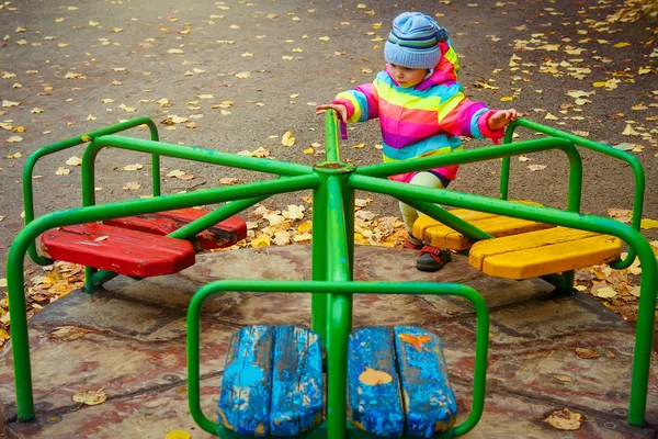 Lilla kid flicka som leker på karusellen. barn rider karusell i lekplats under hösten. — Stockfoto