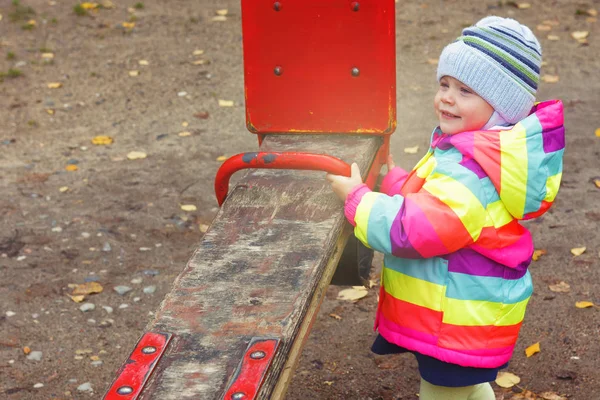 Bambino sta giocando sul parco giochi con altalena. Piccola ragazza caucasica in autunno nel parco . — Foto Stock