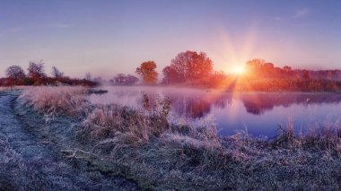 Sonbahar soğuk niteliğine gündoğumu. Manzara nehir üzerinde parlak şafak. güneş ışıkları parlayan hoarfrost ile çimen