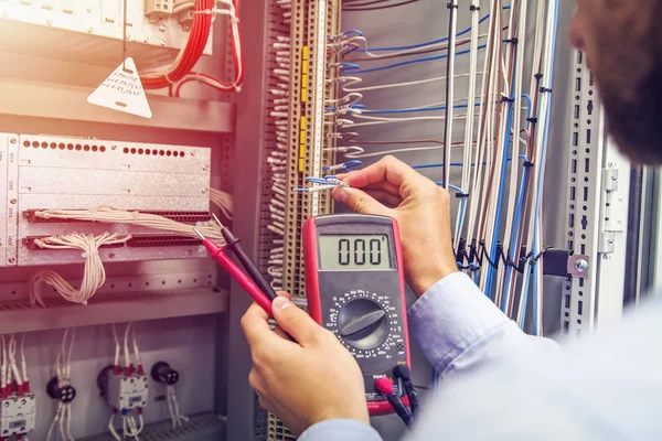 Engineer tests industrial electrical cabinet. Wire in hand of electrician with multimeter. Professional in control panel of industrial equipment.