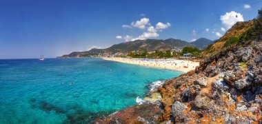 Alanya, Türkiye'de kayalık plajı ile cennet tropikal lagün. Deniz ve dağlar manzarada güneşli yaz günü. Alanya plaj panoramik manzarası. Tropik sahil şeridi üzerinde taşlarla defne.