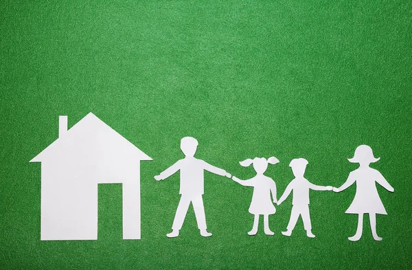 Concepto de familia y hogar. Padres e hijos tomados de la mano. Figuras familiares de papel y casa sobre fondo textural verde —  Fotos de Stock