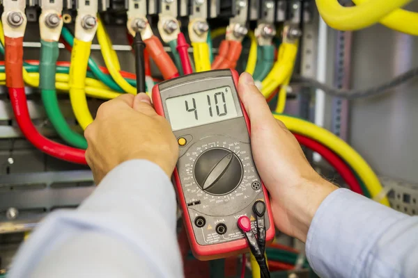 Multimeter in hands of electrician in power high voltage three phase circuit box close-up. Engineer hands with tester measured. Electric fuse panel. — Stock Photo, Image