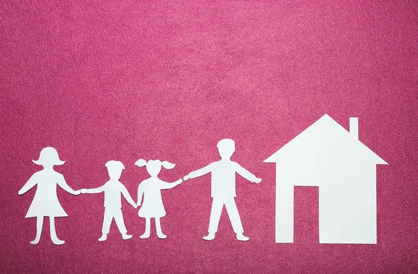 Paper figures of family holding hands near house. Happy family and home concept. Parents and children's on pink background — Stock Photo, Image