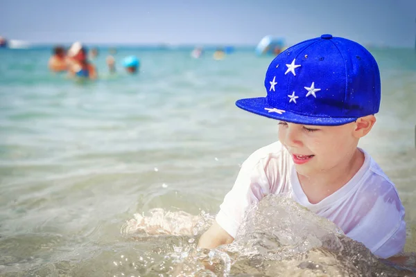 Anak laki-laki kaukasia sedang mandi di air laut di pantai melawan orang-orang berenang di atas kuda. Liburan musim panas di hari yang cerah. Liburan tropis dengan cabe — Stok Foto