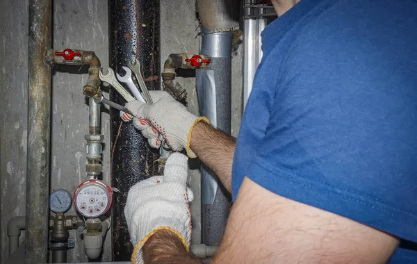 Plombier répare les tuyaux et la plomberie. Travailleur professionnel avec clé à molette sur fond de tuyaux d'égout, manomètres et mélangeurs . — Photo