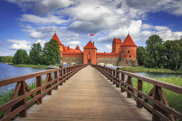 Zamek w Trokach na Litwie w jasny, słoneczny dzień z błękitnego nieba i białe chmury. Krajobraz Zamek z mostu przez jezioro. Zamek na wyspie. — Zdjęcie stockowe