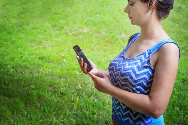 Young woman with modern smartphone in green park background — Stock Photo, Image