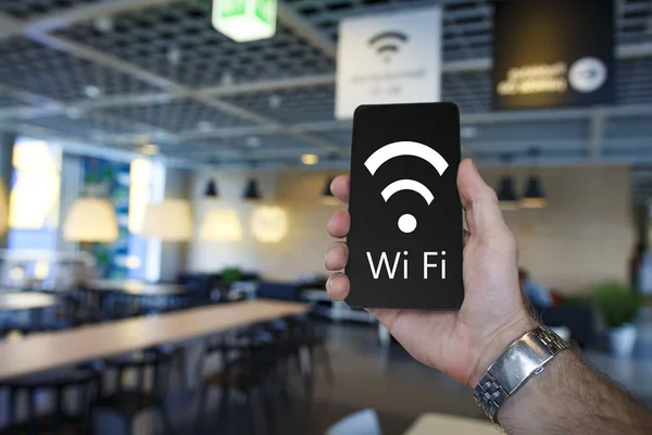 Darmowe Wi-Fi. Nowoczesny smartfon w ręce człowieka w kawiarence z darmowym wifi. Podłączanie smartfona do strefa Wifi w przytulnej kawiarni człowiek. Odznaka i napis wi fi w telefonie czarny — Zdjęcie stockowe
