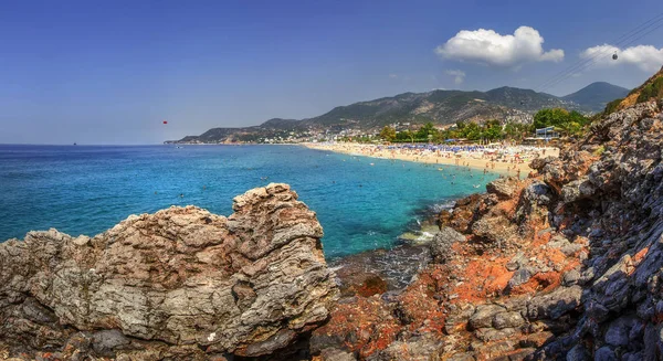 Rocky Dağları ve güneşli yaz gününde mavi deniz deniz manzarası. Panoramik manzara Alanya Beach, Türkiye. Tropikal resort yaz tatili. Cennet lagün sahilde turistler ile defne.
