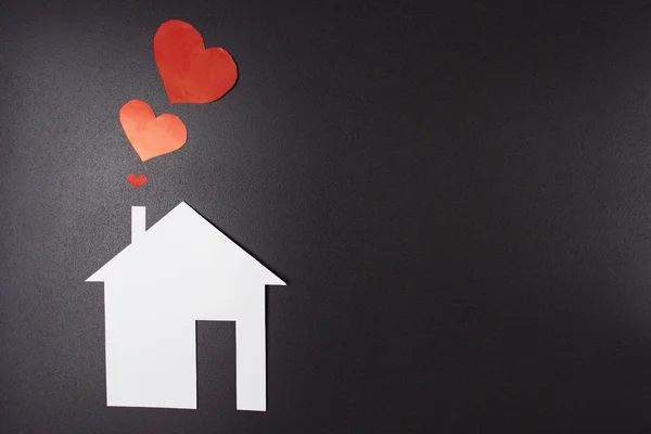 Casa di carta bianca con cuori rossi da camino su sfondo nero. Concept house. Assicurazione e sicurezza degli alloggi. Amore, famiglia e casa . — Foto Stock