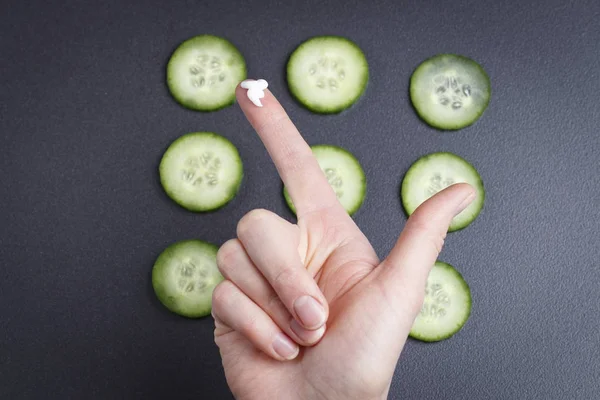 Preparação de máscara facial com pepinos. Mão de mulher com nata no dedo contra o contexto de partes de pepinos. Máscara com pepino de beleza de pele de cara . — Fotografia de Stock