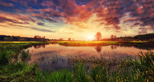 Spring landscape of bright sunrise over river with colorful cloudy sky on horizon. Scenery spring nature